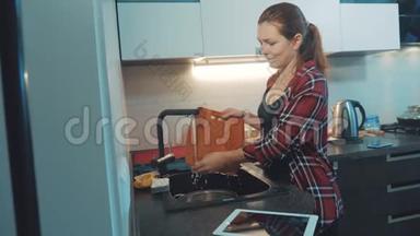 女孩在<strong>厨房</strong>的<strong>砧板</strong>上洗碗，看着一台数字平板电脑。 女人在<strong>厨房</strong>做饭。 女孩洗了一个
